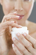 A middle-aged woman holding a pot of moisturising cream