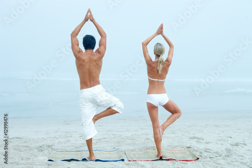 Young man and woman practicing yoga at the beach
