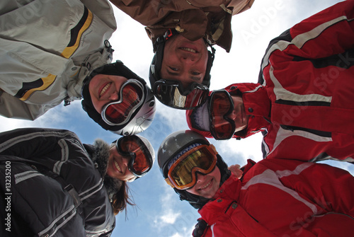Photo: Small group of smiling snowboarders standing in huddle. Small group of smiling snowboarders standing in huddle.