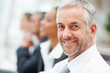 Confident mature business man with other staff at the back Confident mature business man with other staff at the back