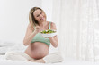 Pregnant woman in bed eating salad