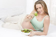 Pregnant woman in bed eating salad