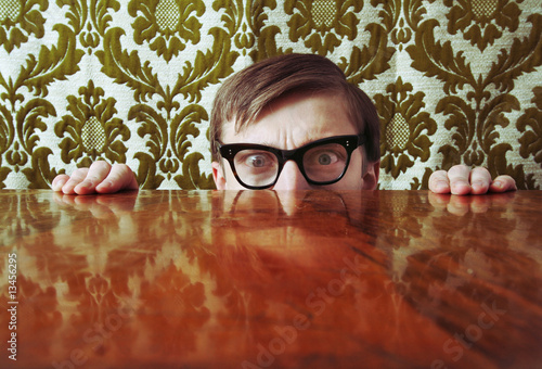 Photo: Scared nerd hiding behind a desk Scared nerd hiding behind a desk