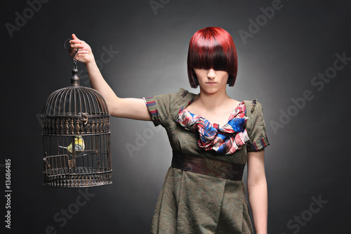Photo : A beautiful young girl holding a birdcage with a bird inside A beautiful young girl holding a birdcage with a bird inside