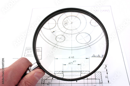 Photo: Reviewing technical drawing. Focus on magnifying glass. Reviewing technical drawing. Focus on magnifying glass.