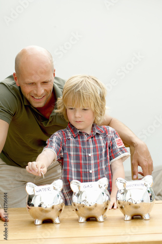 Photo: Father and son putting coin in piggy bank, Den Haag, Netherlands Father and son putting coin in piggy bank, Den Haag, Netherlands