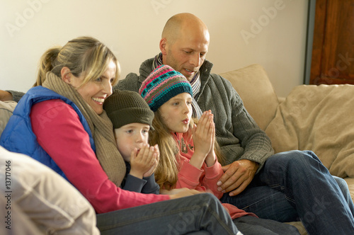Photo: Family in winter clothes keeping warm together on sofa Family in winter clothes keeping warm together on sofa