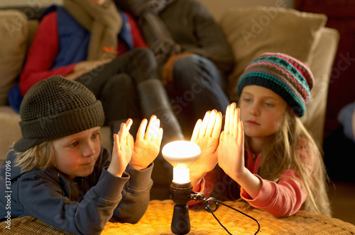 Photo: Family in winter clothes warming hands with a light bulb Family in winter clothes warming hands with a light bulb
