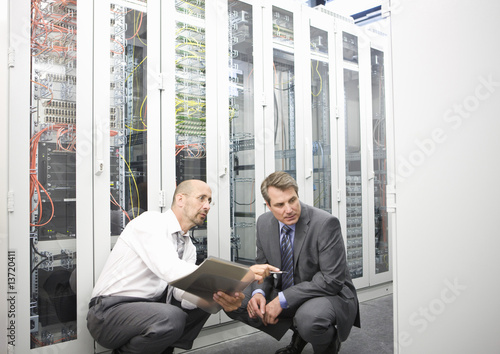 Photo: Two mature men crouching down in a computer server room Two mature men crouching down in a computer server room