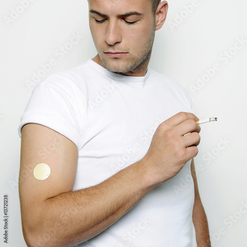 Photo: Young man wearing a nicotine patch and smoking, studio shot Young man wearing a nicotine patch and smoking, studio shot