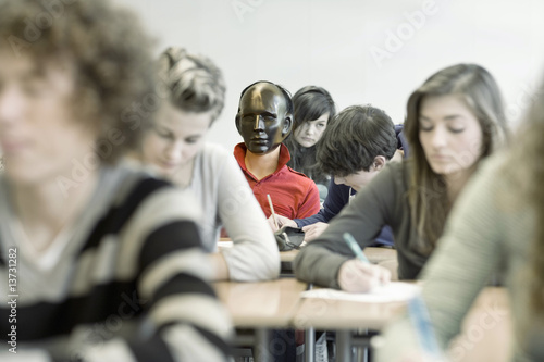 Photo: Classroom full of students working, one in middle with mask on Classroom full of students working, one in middle with mask on