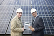 Mature businessmen holding a calculator in front of solar paneling, Munich, Bavaria, Germany