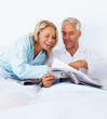 Portrait of an old couple in bed reading the morning newspaper