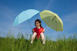 Girl sitting on green meadow holding umbrellas