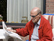 Photo: Pensioner with sunglasses reading newspaper in garden Pensioner with sunglasses reading newspaper in garden