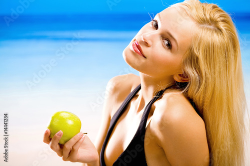 Photo: Young woman with apple in bikini on beach Young woman with apple in bikini on beach