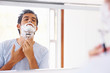 Young man shaving his beard on white background