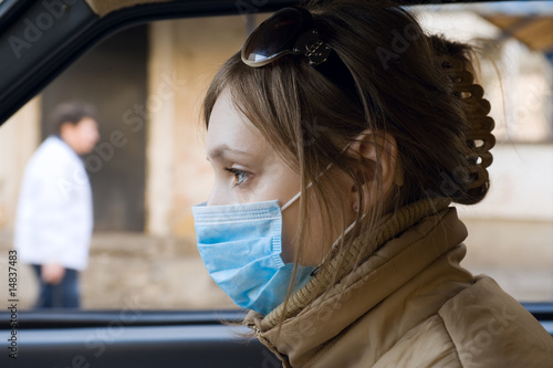 Photo: Young woman travels on automobile in a protective mask Young woman travels on automobile in a protective mask