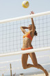 Photo: Female beach volleyball player jumping to spike volleyball over net Female beach volleyball player jumping to spike volleyball over net