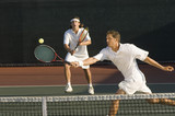 Photo: Tennis Player stretching, Swinging at Ball near tennis net, doubles partner standing behind Tennis Player stretching, Swinging at Ball near tennis net, doubles partner standing behind