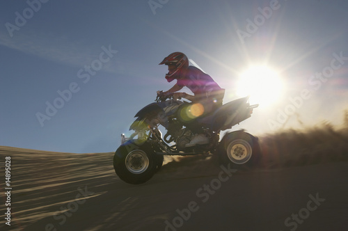 Photo: Man riding quad bike in desert against sun Man riding quad bike in desert against sun