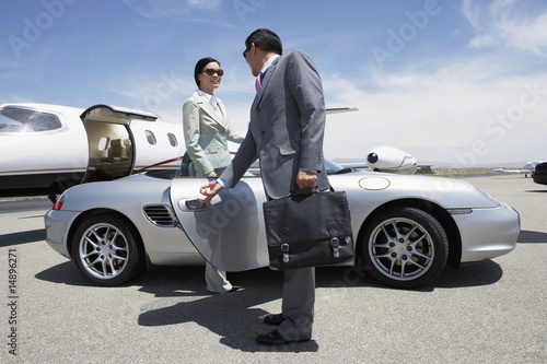 Photo: Businessman holding door of convertible for colleague on landing strip near private jet Businessman holding door of convertible for colleague on landing strip near private jet