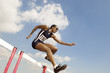 Female athlete jumping hurdle