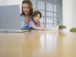 Girl 3-4 colouring in book beside mother using laptop, in home