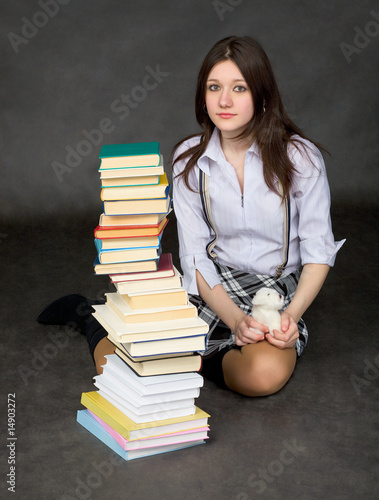 Photo: The beautiful schoolgirl sits near a pile of books The beautiful schoolgirl sits near a pile of books