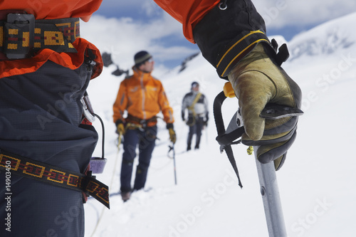 Photo: Hikers using walking sticks in snowy mountains, mid section on front man Hikers using walking sticks in snowy mountains, mid section on front man