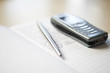 Still life of mobile phone and silver pen resting on notebook