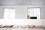 Photo: Female office worker using computer in office cubicle behind trays with documents Female office worker using computer in office cubicle behind trays with documents