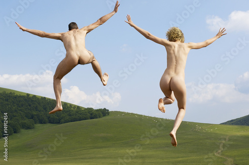 Photo: Young naked couple running and jumping in mountain field, back view Young naked couple running and jumping in mountain field, back view