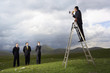 Businessman in mountain field Speaking Through Megaphone to other businessmen, full length