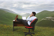 Businessman with feet on desk in mountain field talking on phone, side view
