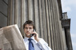 Businessman Reading Newspaper and Talking on Cell  Phone outside building