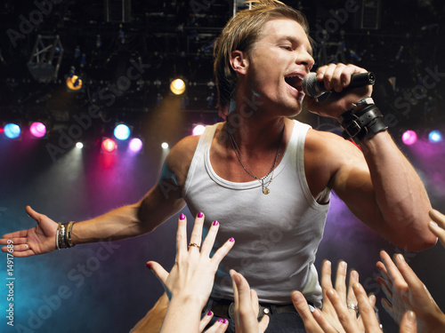Photo: Young Man Singing on stage in concert close to adoring fans, low angle view Young Man Singing on stage in concert close to adoring fans, low angle view