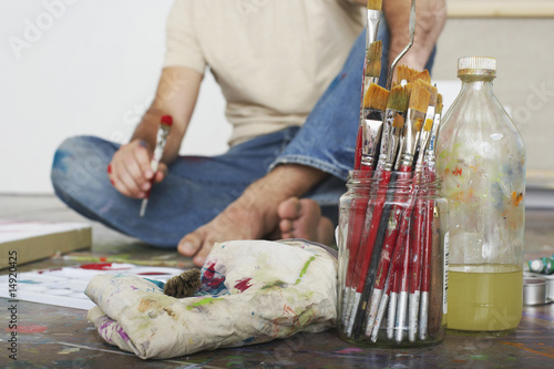 Photo: Artist sitting on floor, focus on paint brushes and materials Artist sitting on floor, focus on paint brushes and materials
