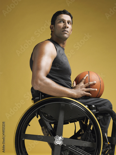 Photo: Paraplegic athlete sitting in wheelchair holding basketball, side view Paraplegic athlete sitting in wheelchair holding basketball, side view