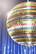 Multi-coloured disco ball in front of blue stage curtain, cropped