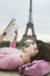 Photo: France, Paris, Young woman reading book on balcony with Eiffel Tower in distance France, Paris, Young woman reading book on balcony with Eiffel Tower in distance