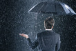 Businessman staying dry under umbrella during downpour, back view