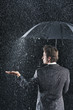 Businessman sticking hand out from under umbrella to feel rain, back view