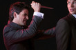 Man stabbing another man in back against black background