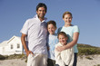 Family standing on beach smiling, beach house behind