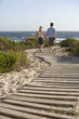 Boy and girl walking hand in hand, along boardwalk toward sea, back view