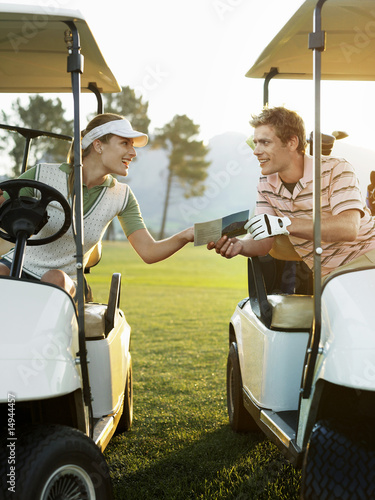 Photo: Young golfers sitting in golf cart, holding score card Young golfers sitting in golf cart, holding score card