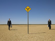 Two businessmen with briefcases walking towards road sign in desert, full length