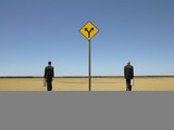 Photo: Two businessmen with briefcases in desert, back view, road sign in foreground Two businessmen with briefcases in desert, back view, road sign in foreground
