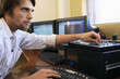 Man using computer keyboard and adjusting knob on mixer.